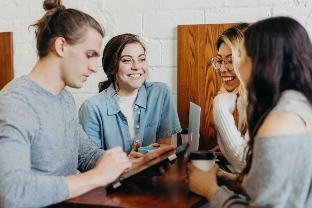 four young people smiling over coffee and electronics
