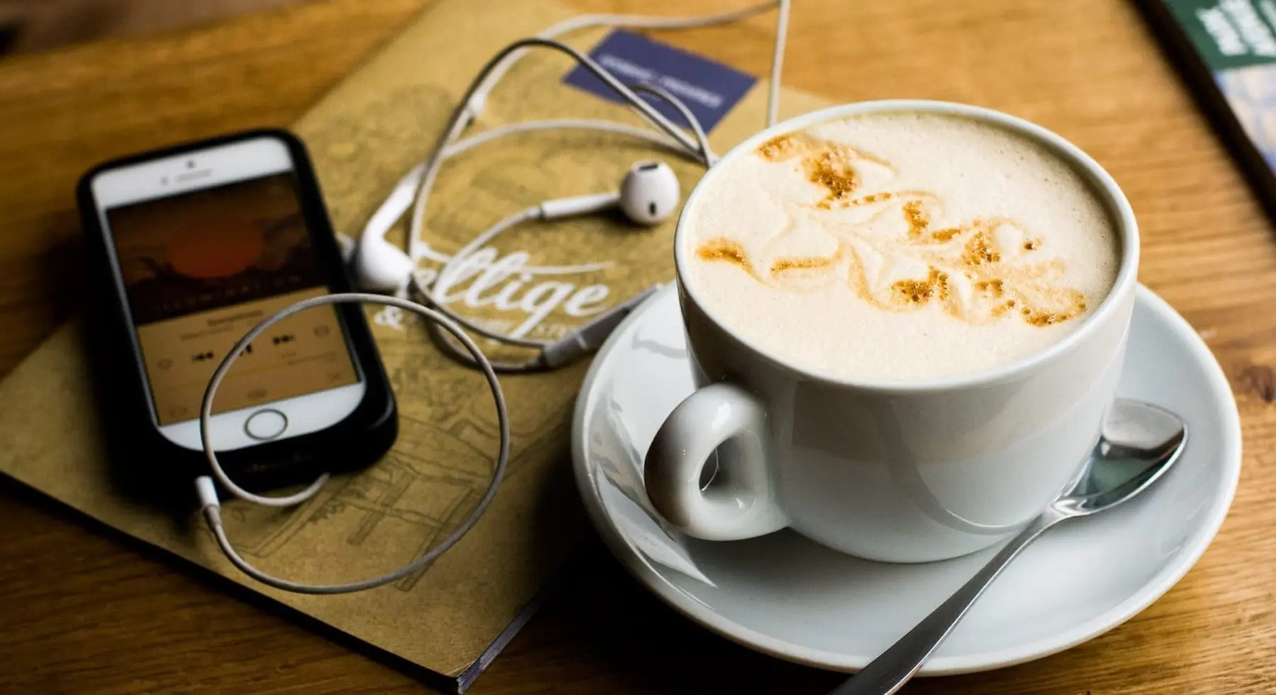 a cup of coffee on top of table with notebook and mobile phone