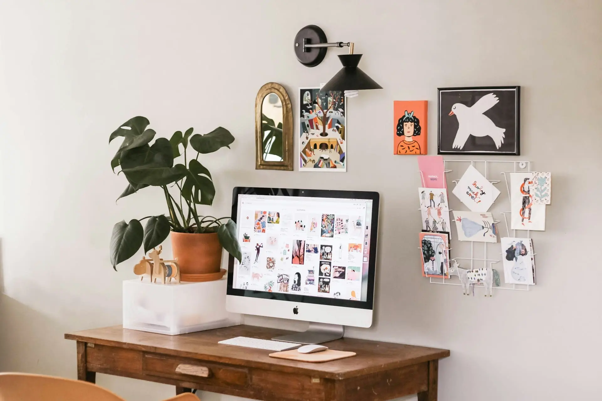 silver imac on top of wooden desk with plants and frames hanging on the wall