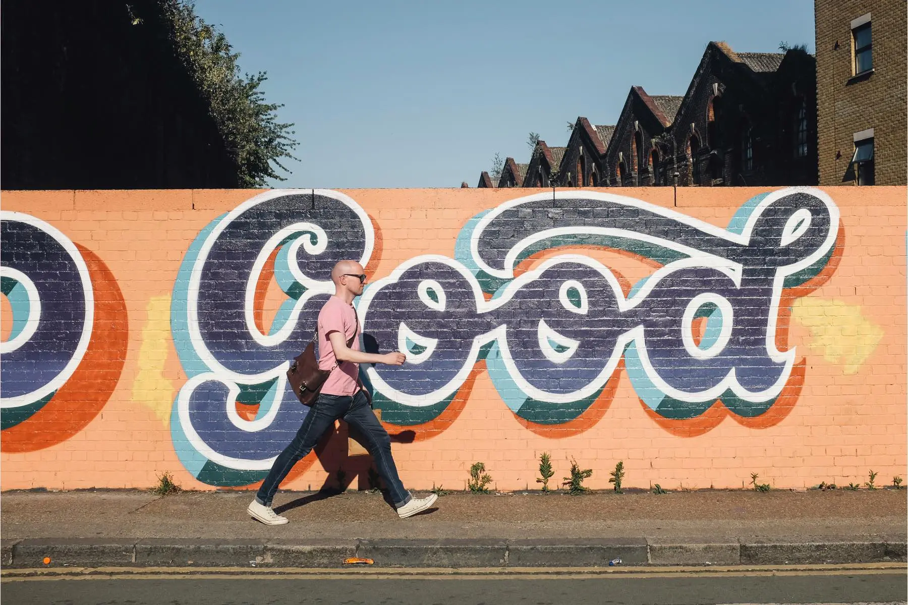 Man walking in front of mural painted with the word "good" in script lettering