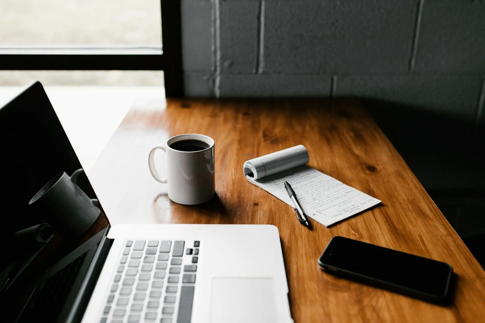 a macbook on top of desk with coffee and notepad
