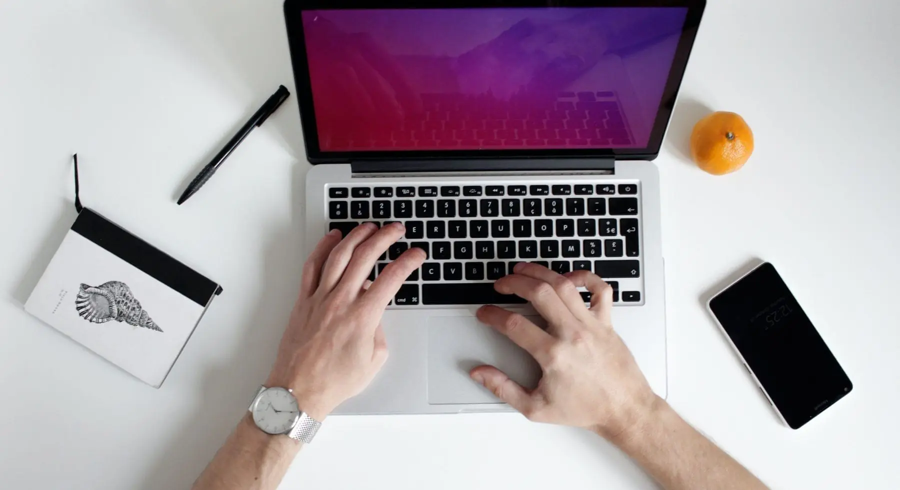a person typing on a laptop with a notebook beside